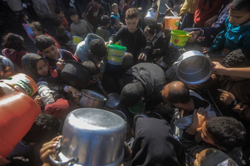 Palestinians gather with pots to receive food at a donation point provided by a charitable organization in Rafah in the southern Gaza Strip. Mohammed Talatene/dpa